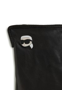 Svart läderväska med strukturerad yta, prydd med en silver- och svart tecknad knapp av en person med solglasögon.