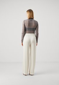 Haut à manches longues à carreaux gris avec un col haut, associé à un pantalon large blanc taille haute, vu de dos.