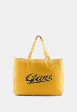Borsa tote gialla con grande logo vintage nero "Gant", forma rettangolare, materiale in tessuto e due manici corti.