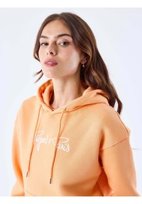Oranje hoodie met trekkoorden, met een witte "Project x Paris" logo. Glad materiaal, relaxed fit en een ontwerp met een buidelzak.