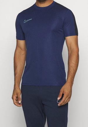 Torse masculin portant un t-shirt Nike bleu marine à manches courtes avec un petit logo Nike bleu clair sur la poitrine et une bande noire sur l'épaule.