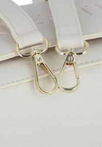 Borsa in pelle bianca testurizzata in primo piano con due ganci in metallo dorato attaccati alle cinghie, che mettono in risalto finiture lisce e linee pulite.