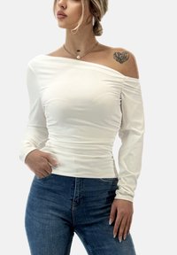 Hvid off-shoulder top med lange ærmer, rynket tekstur, tætsiddende silhuet. Båret med høj-taljede blå jeans.