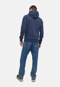 Granatowy hoodie wykonany z mieszanki bawełny, charakteryzujący się luźnym krojem i ściągaczami, zestawiony z jasnoniebieskimi dżinsami i szarymi butami.