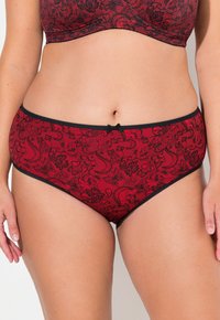 Rode ondergoed met zwart bloemenpatroon, elastische tailleband en een klein zwart strikje in het midden aan de voorkant. Glad, rekbaar materiaal.