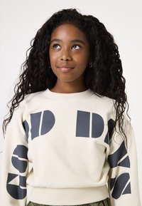 Lichtbeige sweatshirt met donkerblauwe grafische letters en vormen op de mouwen. Ribgebreide manchetten en zoom, met een relaxed fit.