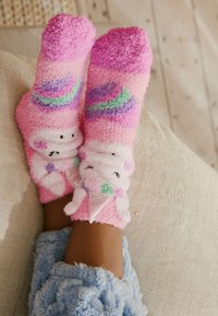Różowe, puszyste skarpetki z uroczym wzorem jednorożca, ozdobione kolorowymi wzorami i teksturowanym wykończeniem. Dodatkowo zdobione detalem w postaci rożka lodowego.