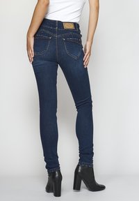 Smala jeans i mörkblå denim med sydda bakfickor och en märkesläderlapp. Bärs med svarta klackboots som går precis över ankeln.