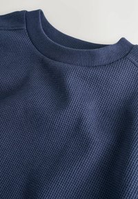 Maglione a coste blu navy con scollo rotondo, che presenta una superficie strutturata e un leggero effetto elasticizzato, progettato per il comfort.