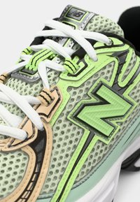 Groene mesh sneakers met zwarte en beige accenten, witte veters en een gestructureerd "N"-logo. Opvallende details zijn het contrasterende stiksel.