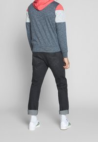 Hoodie med blå kropp och röda, grå och vita ränder på ärmarna. I kombination med mörka jeans med uppvikta ärmar och vita skor.