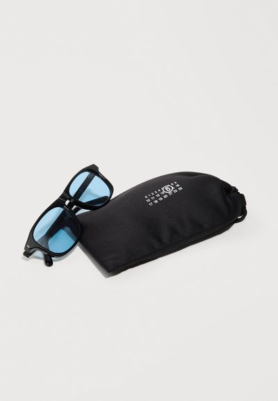 Γυαλιά ηλίου με μαύρο πλαίσιο και φακούς με μπλε απόχρωση, τοποθετημένα δίπλα σε μια μαύρη μαλακή θήκη με λευκούς τυπωμένους αριθμούς και έναν αριθμό 6 μέσα σε κύκλο.