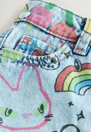 Színes rajzfilmszerű mintákkal díszített farmeranyag, amelyen macska, almák és szivárvány látható. Kontrasztos varrás és gomb részletek is szerepelnek rajta.