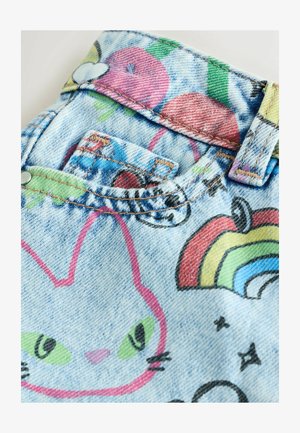 Denim-kangas, jossa värikkäitä sarjakuvakuvioita, sisältäen kissakuvion, omenoita ja sateenkaaren. Sisältää kontrastiväriset ompeleet ja napin yksityiskohdat.