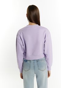 Lawendowy skrojony sweatshirt z opadającymi ramionami, prążkowanym dołem i teksturowanym materiałem, połączony z jasnoniebieskimi, podartymi spodniami o wysokim stanie.