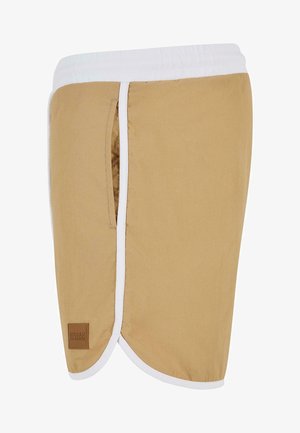 Beesidised lühikesed püksid valge elastse vöökoha ja küljetaskuga, millel on pruun silt. Sile tekstuur, ümmargune alläär ja minimaalne disain.