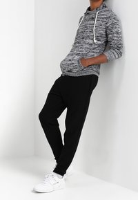 Grau-schwarz gestreifter Hoodie mit Fronttasche und Kapuze mit Kordelzug, kombiniert mit schwarzen Jogginghosen und weißen Sportschuhen.