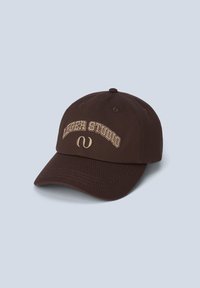 Brown cotton baseball cap featuring curved brim, embroidered text "LEGER STUDIO," and accent logo in beige on the front.