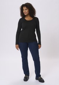 Haut noir à manches longues avec un col en dentelle ondulé, associé à un jean droit bleu foncé et des chaussures noires à semelles épaisses.