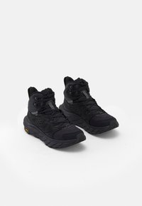 Scarpe da trekking alte nere che presentano un mix di materiali testurizzati, lacci prominenti e una suola resistente con un distintivo accento arancione.