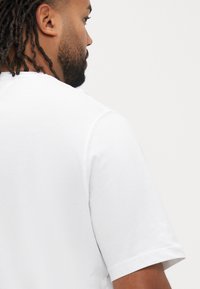 White short-sleeved t-shirt with a crew neckline, featuring a smooth cotton texture and clean stitching along the shoulders and hem.