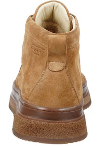 Beige Wildleder-Stiefelette mit abgerundeter Spitze. Gepolsterter cremfarbener Innenraum, braune Gummisohle und Stichdetails. Logo prägung an der Seite.