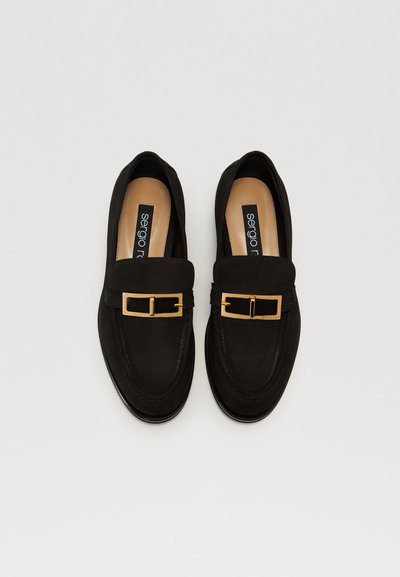 Melnas zamša loafers ar kvadrāta formas zelta sprādzi, noapaļotu purngalu un gludu iekšējo oderi. Viegls dizains ar plakanu zoli.