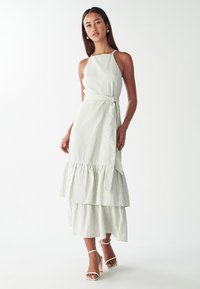 Sukienka midi w paski w jasnym zielonym i białym kolorze, z dopasowanym gorsetem, dekoltem na halter, owiniętym w pasie i warstwowym falbanistym dołem. Elegancka tekstura materiału.