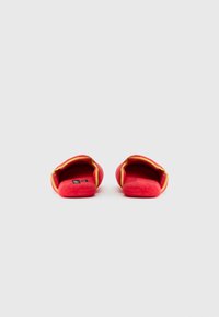 Rode pluche slippers met een zachte textuur, gele bies en een ontwerp met open achterkant. Minimale merkaanduiding zichtbaar op de voetbed. Eenvoudige, gezellige stijl.