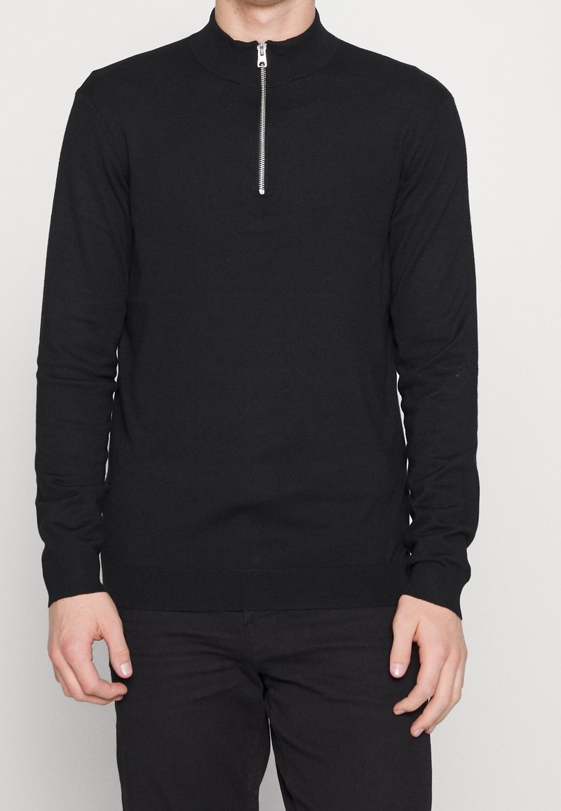 Maglione nero a maniche lunghe con collo alto e chiusura a mezza zip, realizzato in un morbido materiale a maglia. Design aderente, con dettagli di cucitura minimi.