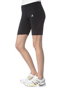 Kvinnliga ben som bär svarta Adidas knälånga träningsshorts och vita Adidas löparskor med guld- och svarta ränder.