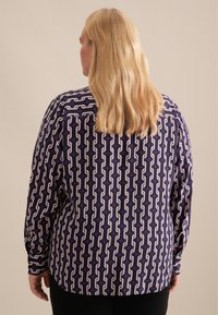 Camicia a maniche lunghe di colore viola con un motivo geometrico bianco. Tessuto liscio con una vestibilità comoda, dotata di orlo dritto e polsini con bottoni.