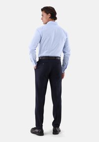 Camicia a righe blu chiaro con colletto classico, abbinata a pantaloni navy scuri. Cintura e scarpe nere completano l'outfit.