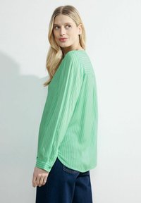Blusa a maniche lunghe a righe verdi realizzata in tessuto leggero con una vestibilità comoda. Orlo curvo e polsini con bottoni. Indossata con jeans scuri.