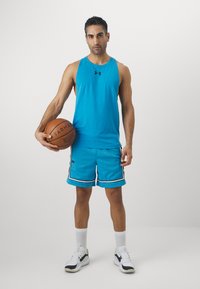 Tyrkis topp med stropper og basketball-shorts med sorte detaljer. Shortsene har en mesh-struktur. Hvite treningsstrømper og svarte sko.