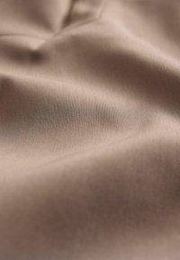 Tejido beige con una superficie suave y ligeramente texturizada, que presenta pliegues sutiles y un patrón de tejido consistente.