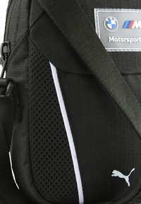 Czarna torba typu messenger wykonana z tkaniny, z siateczkową boczną panelą, białym akcentem w postaci paska oraz logo Puma. Regulowany pasek i teksturowana powierzchnia.