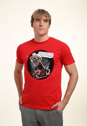 Jeune homme portant un t-shirt rouge avec un chien dessin animé portant des lunettes et de l’équipement, tenant une pancarte indiquant « Ne pas insulter l’autonomie de cet animal. »