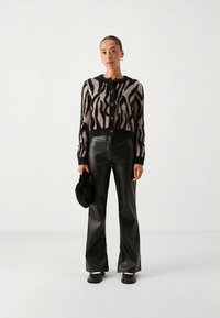 Strikket cardigan i svart og beige sebramønster, med rund hals og knappelukking, kombinert med svarte vide bukser i kunstlær.