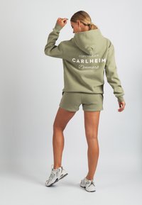 Oliwkowa zielona bluza z kapturem z kieszenią kangurka, nadruk na plecach "COPENHAGEN CARLHEIM Dania", w zestawie z pasującymi szortami i sneakersami.