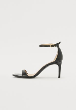 Black leather high-heeled sandal with an ankle strap. Features a smooth texture, open toe, and a thin heel. Gold-toned buckle detail.