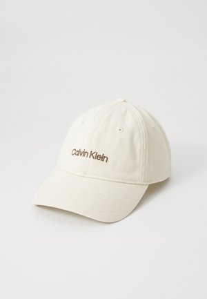 Kremfarget baseballcap laget av bomull med buet skygge, med en brun "Calvin Klein" logo brodert foran. Fem luftehull på toppen.