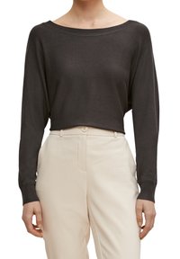 Pull-over en maille gris foncé à manches longues avec un col bateau, coupe courte et poignets côtelés, associé à un pantalon beige clair taillé sur mesure.