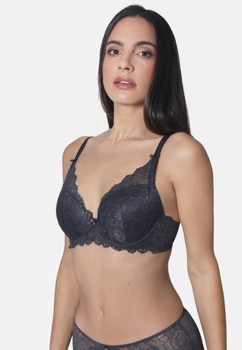 Schwarzer Spitzen-BH mit gepolsterten Cups, floralem Muster, gezacktem Rand, verstellbaren Trägern und einer dekorativen Schleife in der Mitte. Glatter Stoff auf der Rückseite.