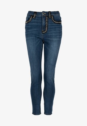 Jean skinny en denim bleu avec garniture cloutée noire le long des poches avant, des passants de ceinture et de la zone de fermeture éclair.