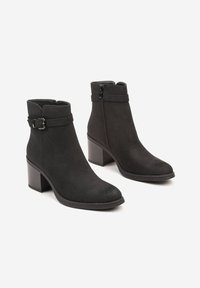 Bottes noires à talon en suède avec une texture lisse, dotées d'une fermeture éclair sur le côté, d'un accent de boucle et d'un talon épais.