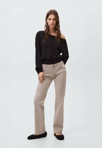 Suéter negro sin hombros con dobladillo acanalado, combinado con jeans rectos de color beige claro con detalles de costura lateral y zapatos negros tipo slip-on.