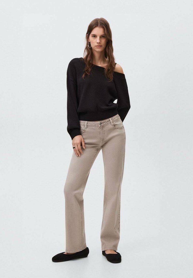 Suéter negro sin hombros con dobladillo acanalado, combinado con jeans rectos de color beige claro con detalles de costura lateral y zapatos negros tipo slip-on.