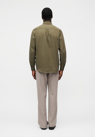Πουκάμισο σε ελιά πράσινο χρώμα με κουμπιά, με στρογγυλεμένο τελείωμα, συνδυασμένο με ανοιχτό μπεζ παντελόνι. Το πουκάμισο έχει μακριά μανίκια και λεπτομέρεια yoke στο πίσω μέρος.