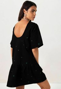 Schwarzes kurzes Kleid mit tiefem Rückenausschnitt, kurzen Ärmeln und einem gestuften Rock mit bunten bestickten Sternmustern.